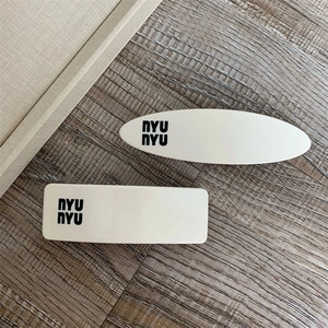 Detail of white acrylic hair clip set featuring black nyu nyu lettering in minimalist style