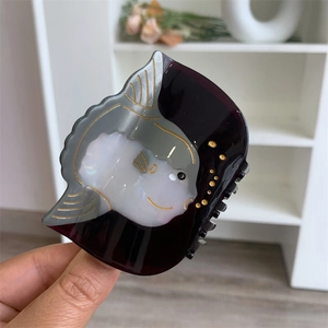 Détail d'une pince à cheveux motif poisson en acétate avec finitions dorées élégantes