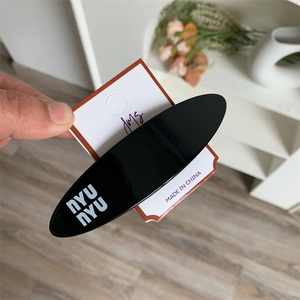 Minimalist black oval hair clip with white nyunyu lettering on a brand display card