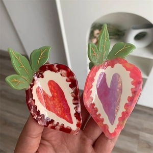 Detail of strawberry hair claw clips featuring heart patterns and green leaf accents