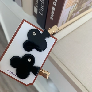 Detail view of two black clover-shaped acetate hair clips with crystal center and gold base