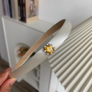 Détail d'un serre-tête en satin champagne avec un zircon jaune carré et des strass