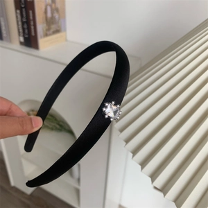 Détail d'un serre-tête en satin noir orné d'un grand zircon carré et de strass brillants