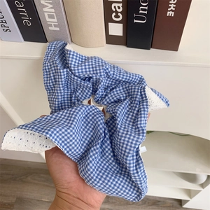 Blue and white plaid scrunchie with lace trim held by hand in a cozy lifestyle setting