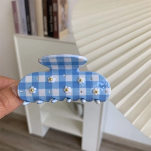 Pinza per capelli a scacchi blu e bianchi con fiori bianchi e strass tenuta in mano