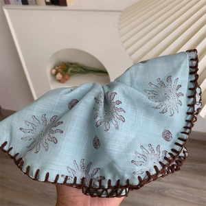 Detail eines hellblauen Leinen-Scrunchies mit Sonnenmuster und Häkelkante