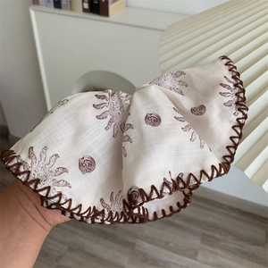 Detail eines cremefarbenen Haargummis aus Leinen mit braunem Muscheldruck und rustikaler Naht