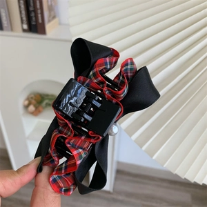 Detail of red plaid fabric bow hair claw clip with pearl accent on black handle