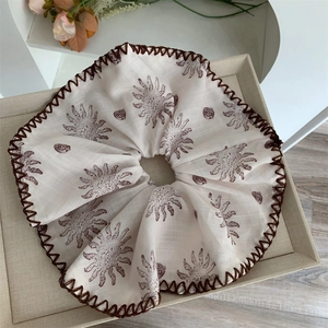 Detailansicht eines beigen Scrunchies mit braunem Wellenrand und Sonnenmustern
