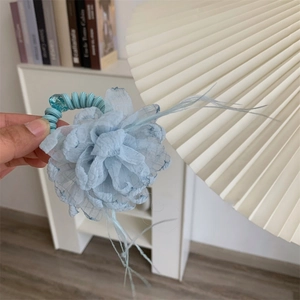 Detail view of light blue chiffon flower hair tie with spiral band and feather tassel