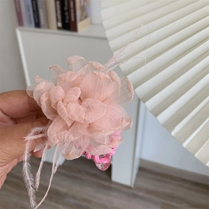 Detailed view of a pink organza flower hair tie with soft feathers and a glitter heart charm