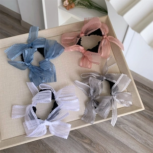 Set of four pastel organza bow hair scrunchies displayed on a beige textured tray