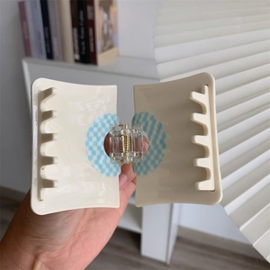 Detail view of cream rectangle hair claw clip with blue checkered pattern and metal spring