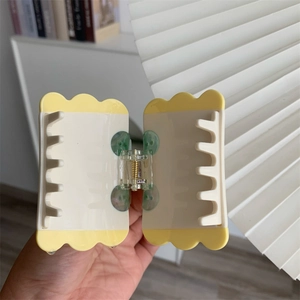 Close-up of cream and yellow square hair claw clip with green button accents and metal spring