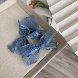 Close-up of dual blue organza bow scrunchies with pleated texture in a beige tray