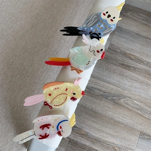 Detailed view of four colorful parrot-shaped acetate hair claws on a display stand