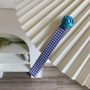 Détail d'une pince à cheveux à carreaux bleus ornée d'une rose en ruban de satin