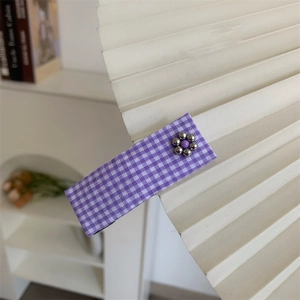 Detail view of purple checkered floral hair clip on decorative white pleated fan