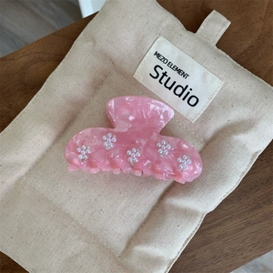 Gros plan d'une pince à cheveux rose marbré avec fleurs en perles et strass délicats