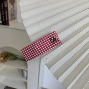 Detailed close-up of a red gingham floral hair clip on a geometric white fan background