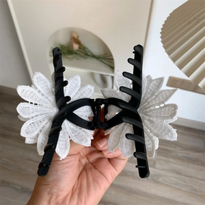 Détail d'une grande pince à cheveux noire ornée de pétales de fleurs en dentelle blanche