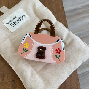 Détail d'une pince à cheveux rose en forme de sac à main avec motifs ours et fleurs