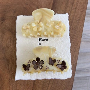 Detail of cream acetate flower and butterfly hair claws with delicate rhinestone accents