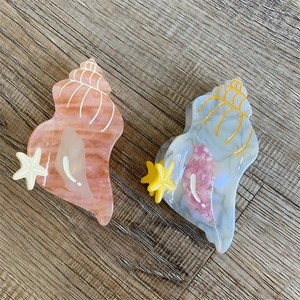 Detail view of two marble textured conch hair claws with starfish accents on wood