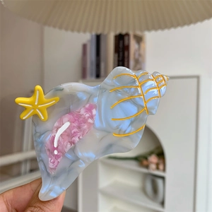 Detailed close-up of a conch shell acetate hair claw clip with a yellow starfish accent