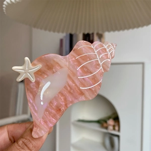 Close-up of pink pearlescent shell hair claw with white starfish detail in a cozy setting