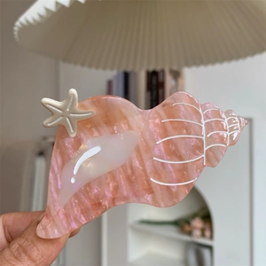 Detail shot of a pink seashell hair claw with pearlescent finish and small starfish decor
