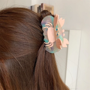 Pink crab hair claw clip made of acetate with blue rhinestones on brown hair bun