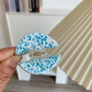 Detail view of acetate hair claw clip featuring blue terrazzo pattern and golden spring