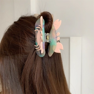 Detail view of a soft pink crab-shaped hair claw clip with colorful gradient finish