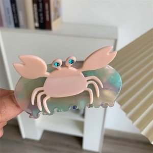 Detailed close-up of a pink crab-shaped hair claw clip with blue rhinestone eyes and gradient base