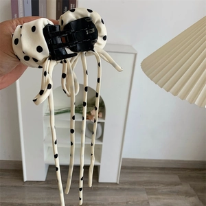 Détail de la pince à cheveux crème à pois noirs avec de longs rubans à franges élégants