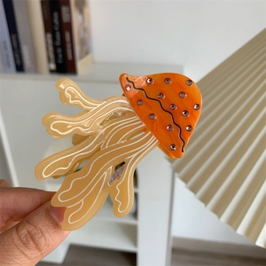 Close-up of jellyfish hair claw clip with orange acetate shell and pink rhinestones
