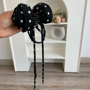 Détail d'une grande pince à cheveux noire avec nœud à pois et longs rubans mousseline