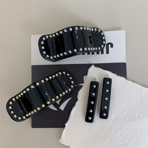 Set de barrettes noires en acétate avec rivets métalliques sur fond de couleur neutre