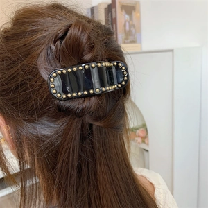 Détail d'une pince à cheveux noire en acétate avec perles dorées sur mannequin