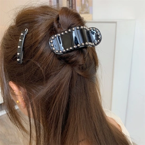 Détail de la pince à cheveux en acétate noir avec bord perlé argenté sur cheveux bruns
