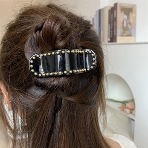 Détail d'une pince à cheveux noire avec perles dorées sur cheveux châtains