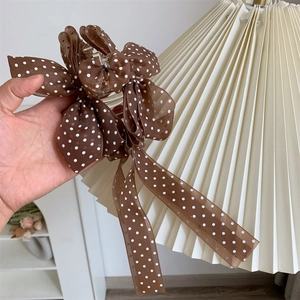 Close-up of brown polka dot bow hair claw clip with long ribbon tassels held by hand