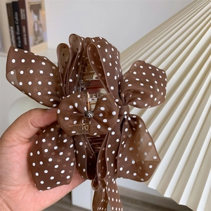 Detail of coffee chiffon polka dot bow hair claw clip with rhinestones hand-held