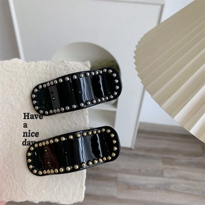 Détail de barrettes en acétate noir avec perles métalliques argentées et dorées sur carte
