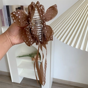 Close-up of a large shark clip featuring a brown polka dot chiffon bow and flowing tassels