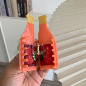 Detail of unique acetate hair claw featuring orange juice bottle design and cherry label