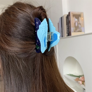 Vue détaillée d'une pince à cheveux papillon bleue sur des cheveux bruns ondulés
