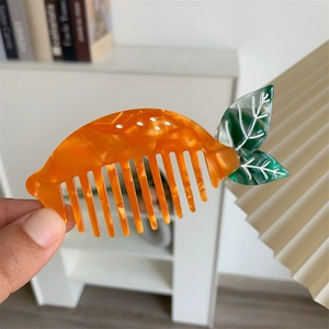 Macro di un pettine creativo in acetato a forma di carota con trama marmorea e foglie verdi