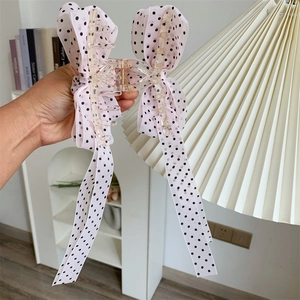 Pink polka dot bow hair claw clip with long ribbons held in a home setting